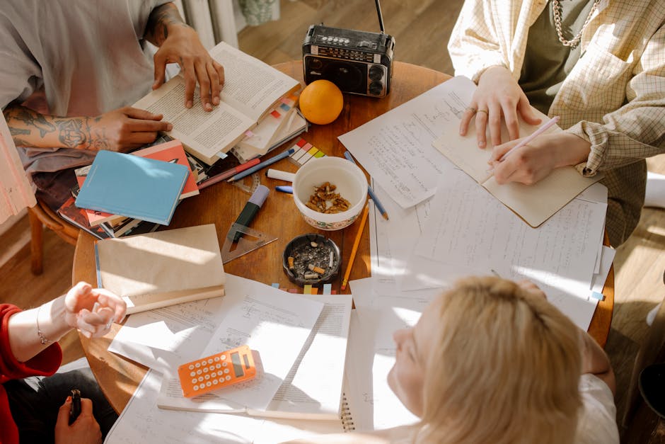 A group of students studying together, taking notes and reading textbooks around a table.